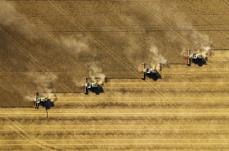 Una veduta aerea di alcune mietitrebbie che lavorano in parallelo per la raccolta di colture in un campo marrone